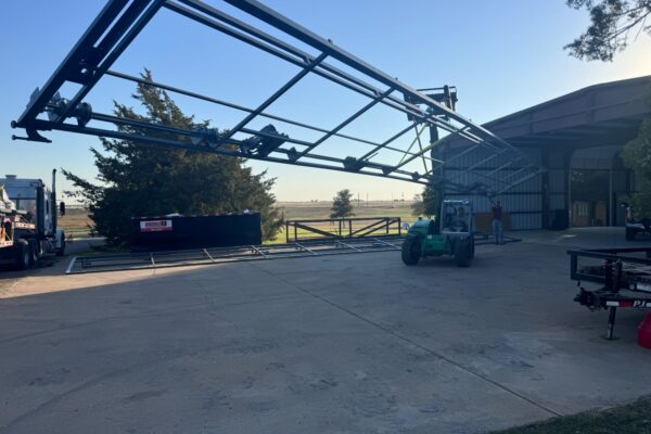 Installation of a large steel bifold airplane hangar door using a forklift for precision placement.