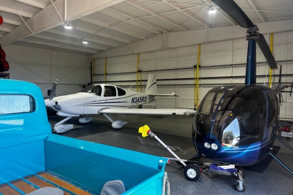 Interior of a metal airplane hangar with a private plane, helicopter, and classic truck.