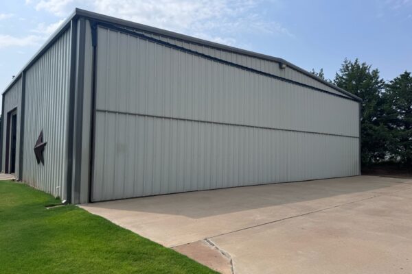 Completed exterior of a custom-built airplane hangar featuring a large bifold door and metal siding.